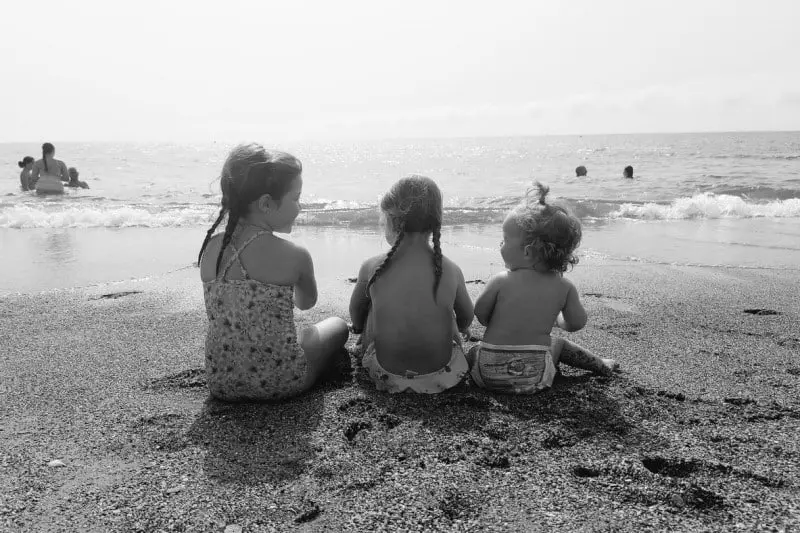 Victoria, con sus hermanas mayores en la playa. La foto es en blanco y negro, están sentadas en la arena delante del mar.