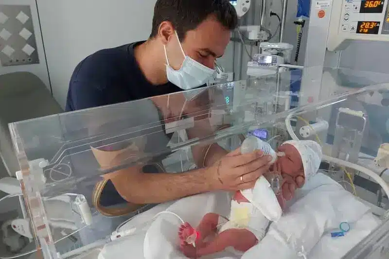 Víctor, con Victoria, en la UCI, poco después del nacimiento de la pequeña. Su papa le esta dando el biberón, Victoria se encuentra dentro de una incubadora